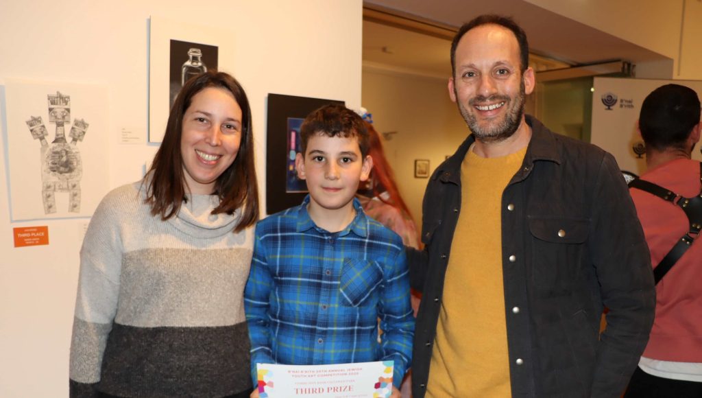 Year 6 student poses with his mother and the Principal Marc Light after receiving a B'nai B'rith award for his art. He is looking at the camera with a serious and proud look on his face. The adults are smiling at the camera.