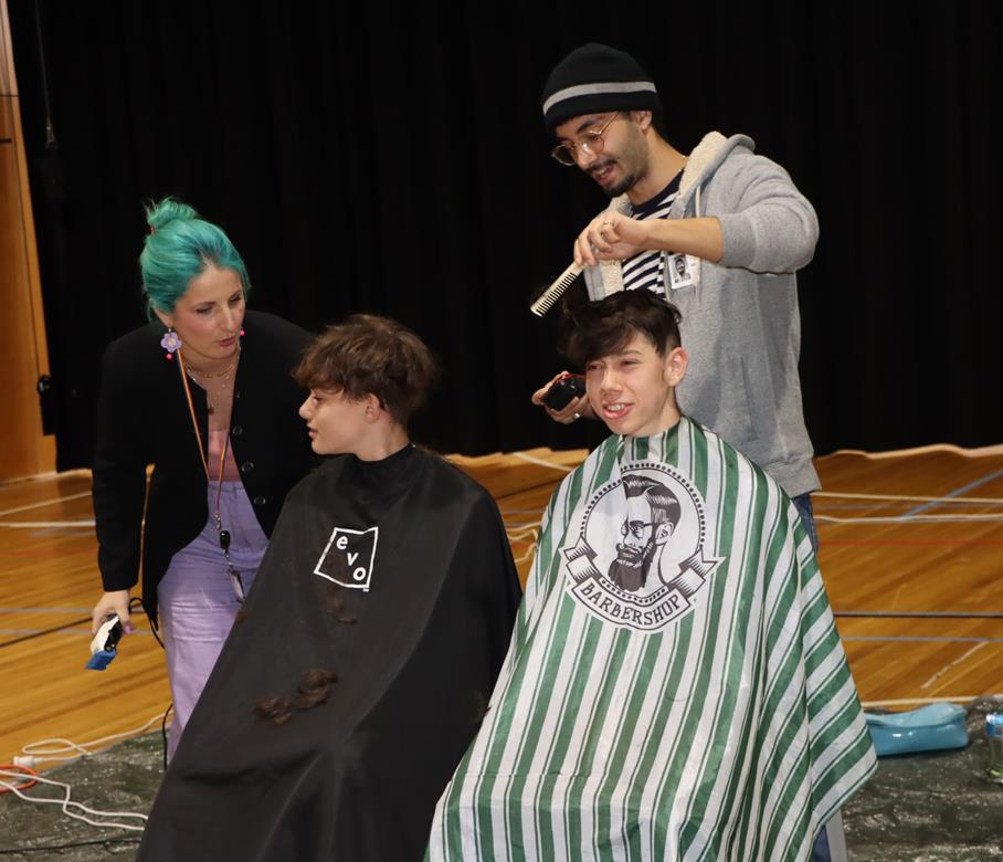 Two students are about to have their heads shaved. They are wearing barber's capes. They are raising money to help cure Leukaemia with the World's Greatest Shave.