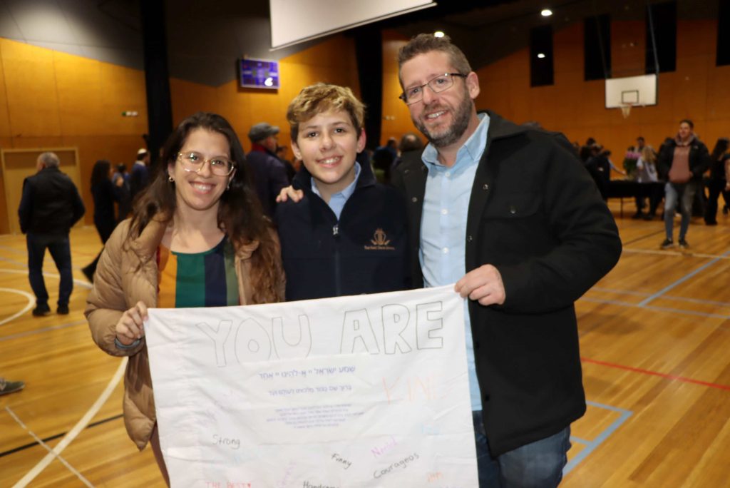 A Year 7 family stands proudly with their son holding a pillowcase that they have decorated together as part of activities around mitzvot. They are happy.