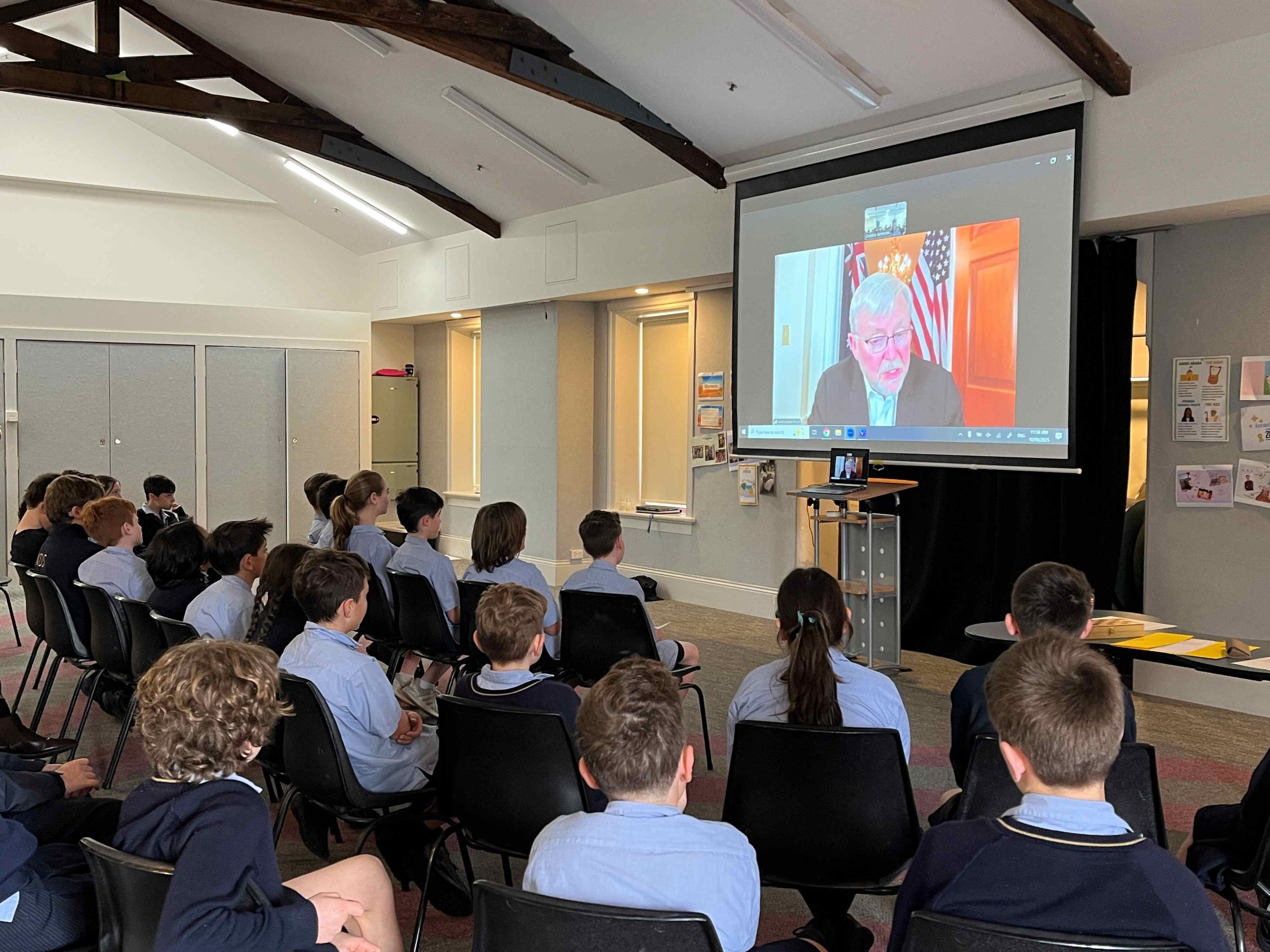 Ambassador Kevin Rudd is on a big screen, talking to Year 5. There is an American and Australian flag behind him.