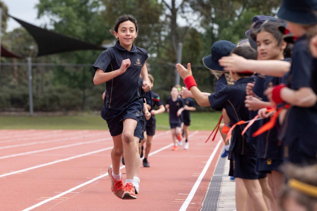 Year 5 student runs on the orange track at the Prep to Year 5 Athletics Carnival, while being cheered on by fellow students.