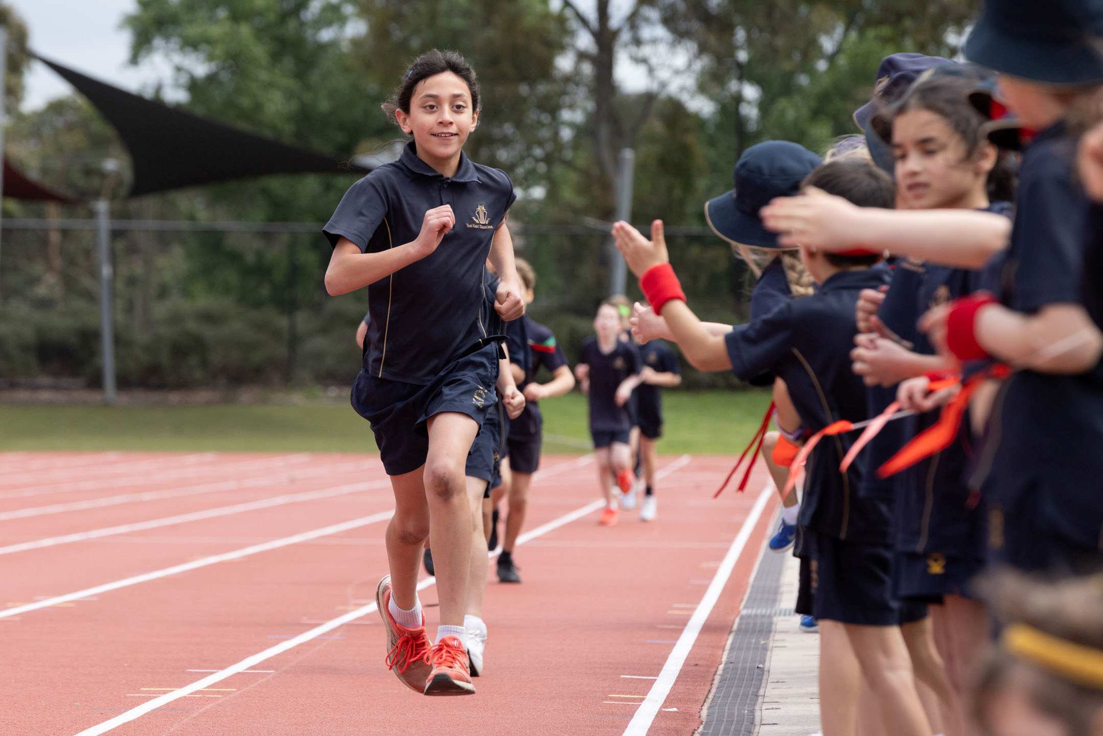 Year 5 student runs on the orange track at the Prep to Year 5 Athletics Carnival, while being cheered on by fellow students.