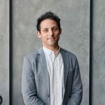 This shows a School Council member posing in front of a grey background, wearing a grey suit. He looks professional and happy.