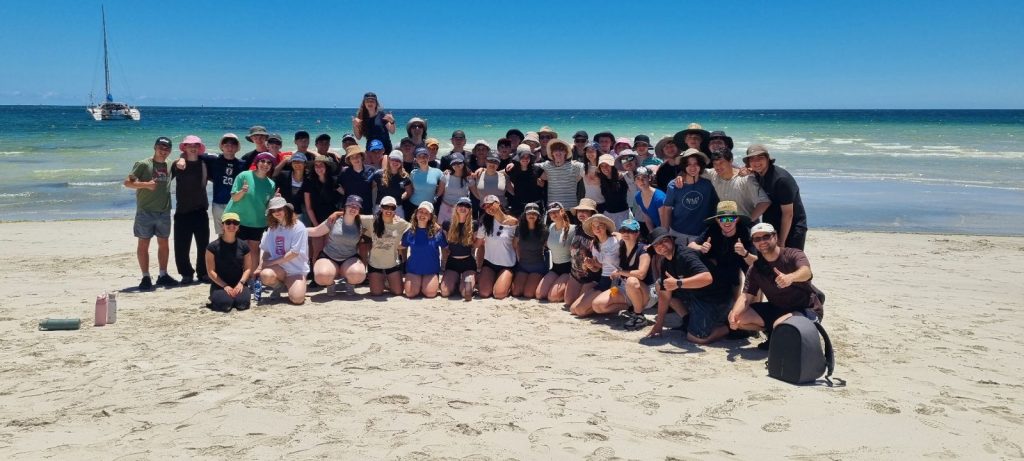 Year 11 students stand on white sand next to the blue sea. They are on camp in Western Australia