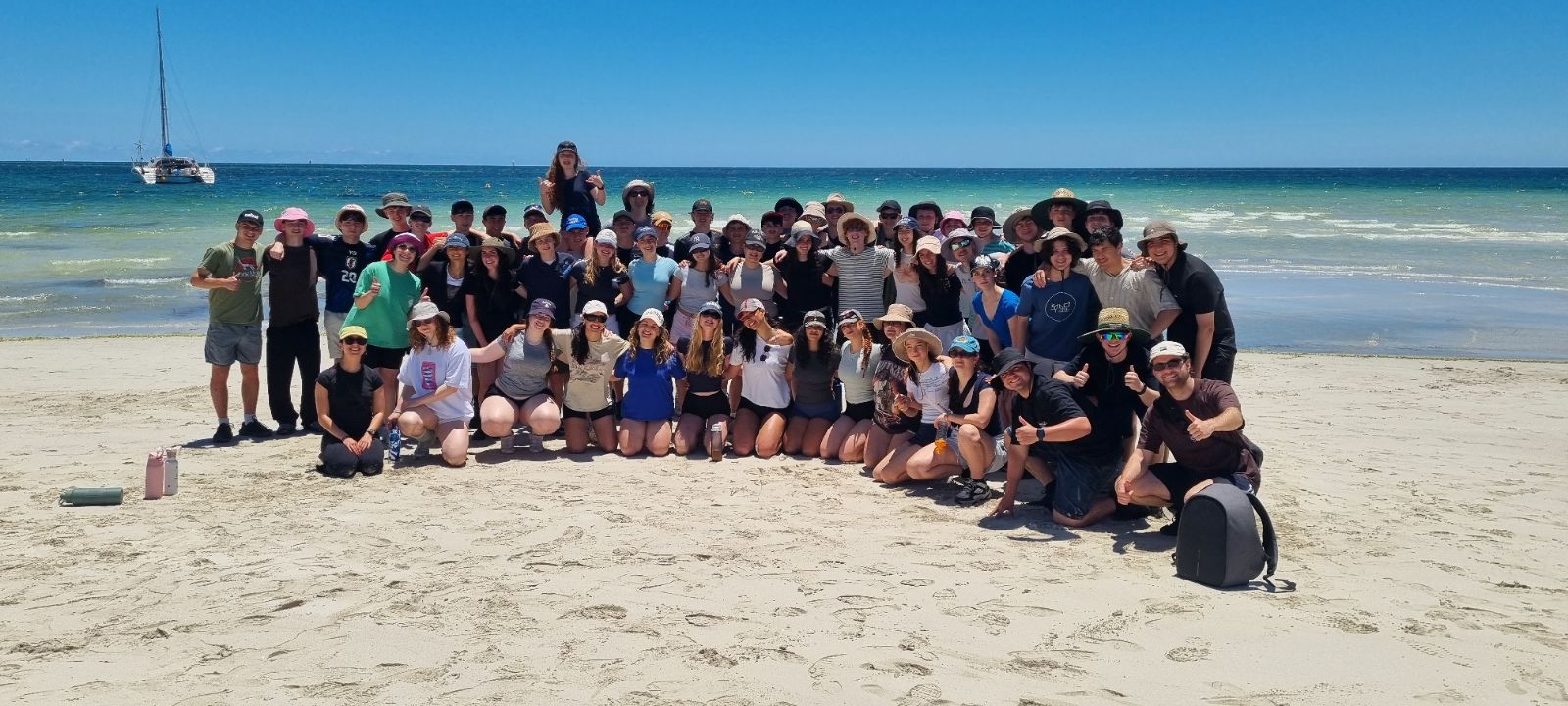 Year 11 students stand on white sand next to the blue sea. They are on camp in Western Australia