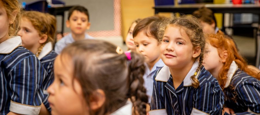 Prep students in the Prep classroom. One girl in plaits looks at the camera and smiles.