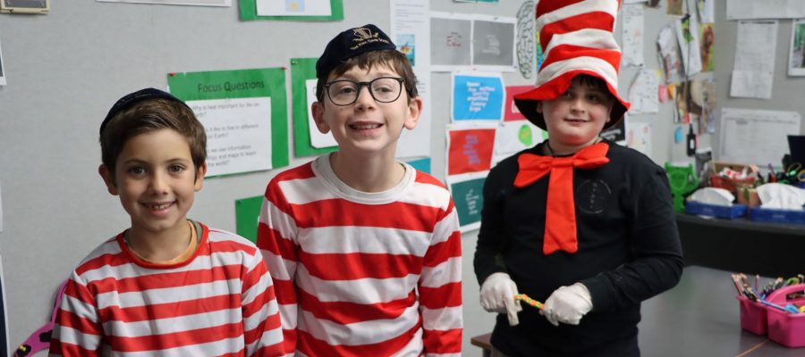 Three Junior School students wearing red and white stripes are looking at the camera and smiling. Two look like Wally from Where's Wally, one student is wearing a tall striped hat like the Cat from the Cat and the Hat by Dr Suess