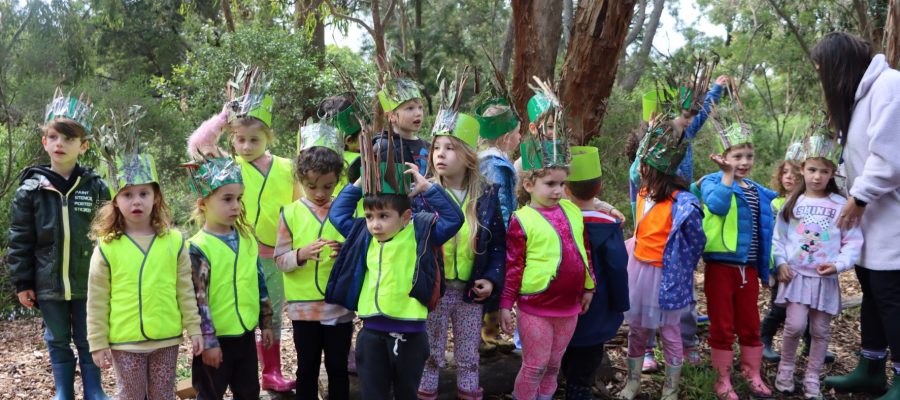 ELC students are in the forest in a group. They are wearing crowns they have made themselves.