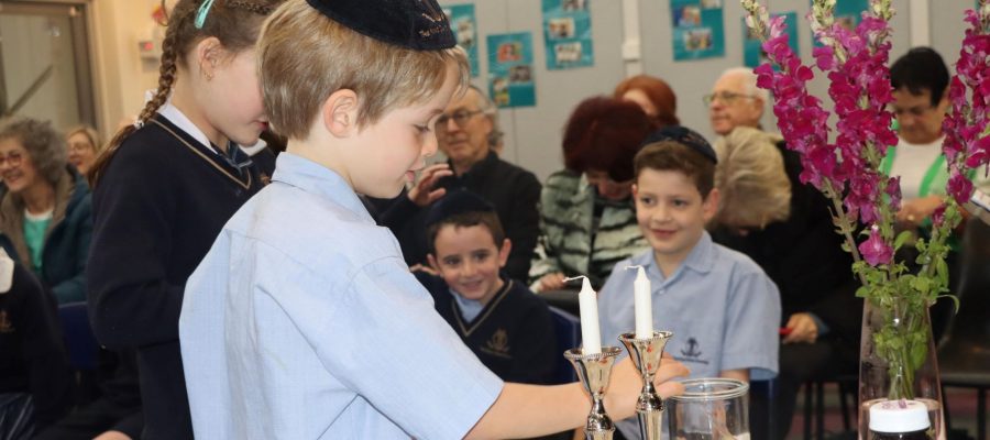 Two children are lighting Shabbat candles, there are children looking at the candles and grandparents sitting down.