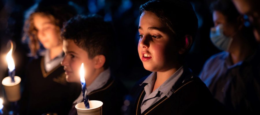 Two students hold Havdalah candles. They are looking down at the candle flames with their mouths open, singing a Havdalah song.
