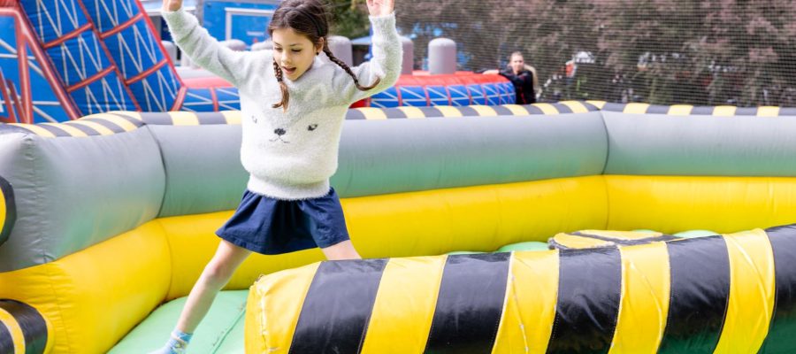 A young girl is playing on a green and yellow inflatable ride at the King's Carnival. She has her arms in the air and is smiling