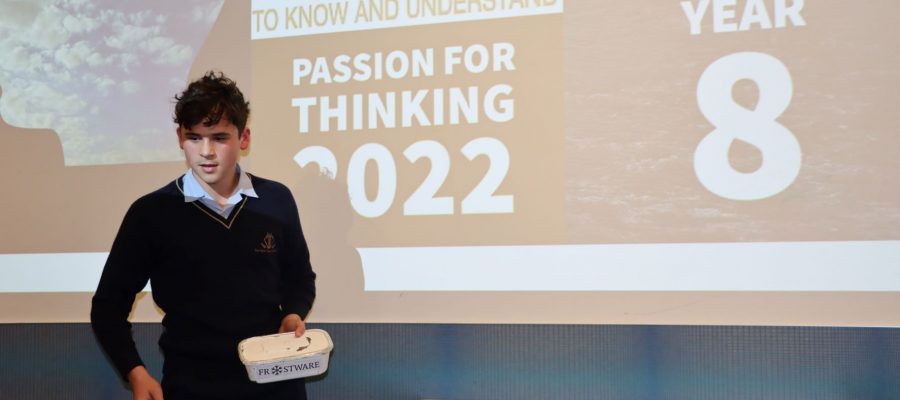 A boy presents his project in front of a screen that says Passion for Thinking