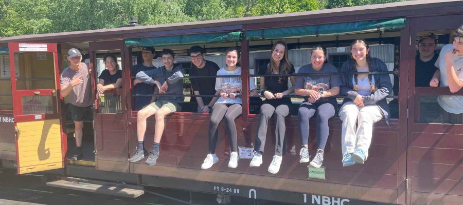 A group of Tourism students are sitting on the Puffing Billy train, they are smiling and waving. They have been investigating sustainable tourism.