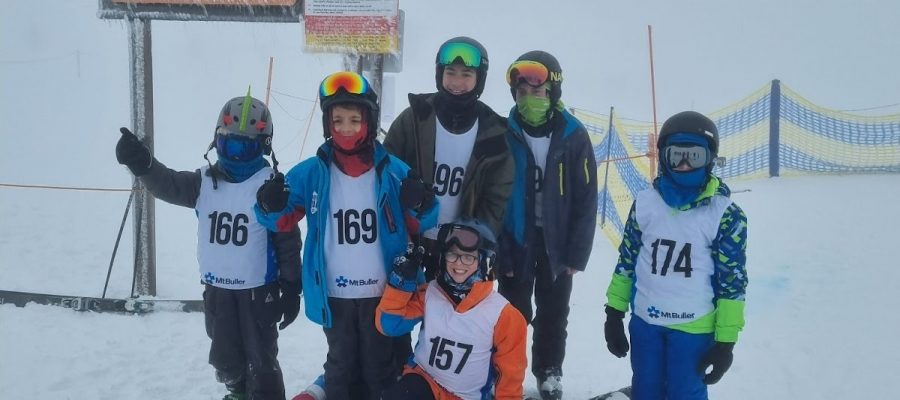Seven students stand in snow, they are dressed in snow gear and are looking at the camera smiling