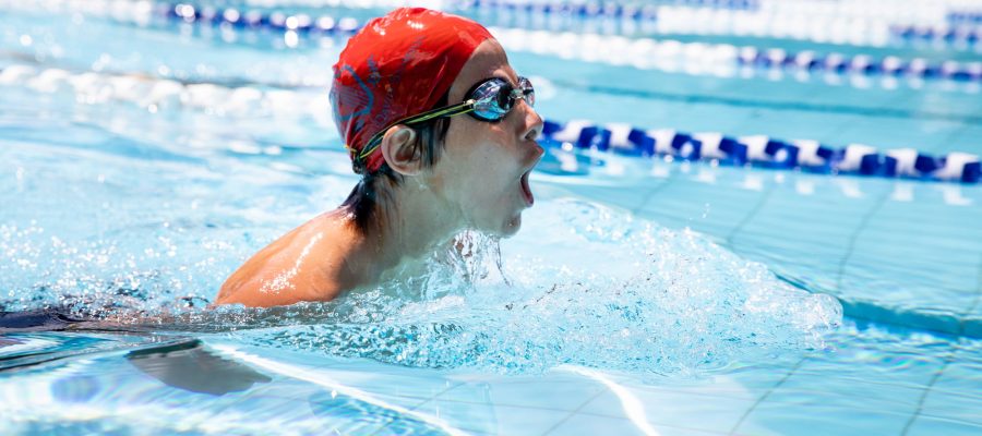 Senior school student wearing a red swimming cap and goggles in a swimming pool splashing water