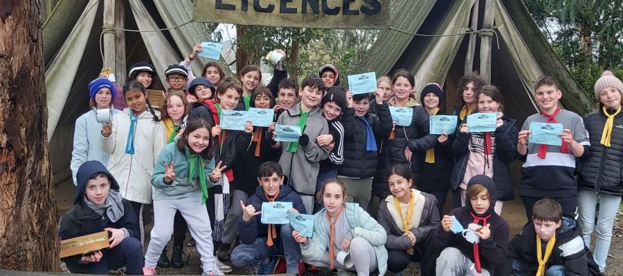 Year 5 students are in front of two old fashioned tents, they are holding mining licenses and smiling at the camera.